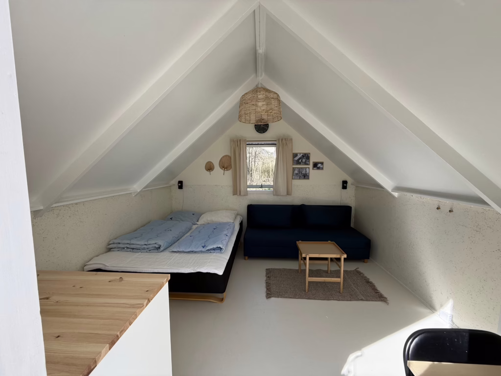 Lille hytte med åben dør og indblik til dobbeltseng